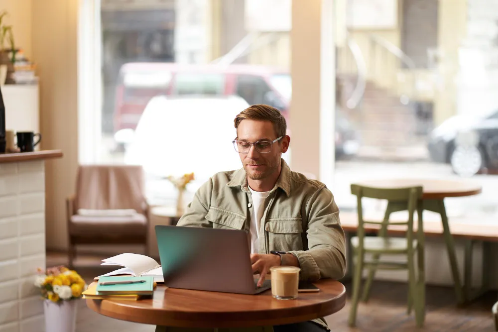 A digital nomad working on a laptop at a beach cafe in Dubai with a "Visa Approved" notification